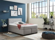 Modernes Boxspringbett in einem stilvoll eingerichteten Raum mit großen Fenstern, seitliche Perspektive.