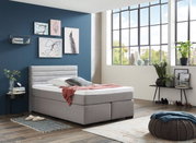 Modernes Boxspringbett in einem stilvoll eingerichteten Raum mit großen Fenstern, seitliche Perspektive.