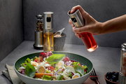 Essig-Öl-Sprüher NEVA in der Hand, der aus der Perspektive von oben auf einen frischen Salat sprüht.