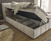 Boxspringbett mit geöffnetem Bettkasten, seitliche Perspektive, zeigt Stauraum mit Decken und Kissen.