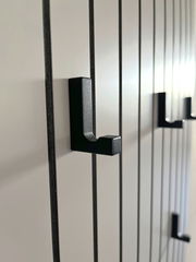 Nahaufnahme eines Garderobenpaneels mit schwarzen Haken auf vertikalen Streifen, seitliche Perspektive.