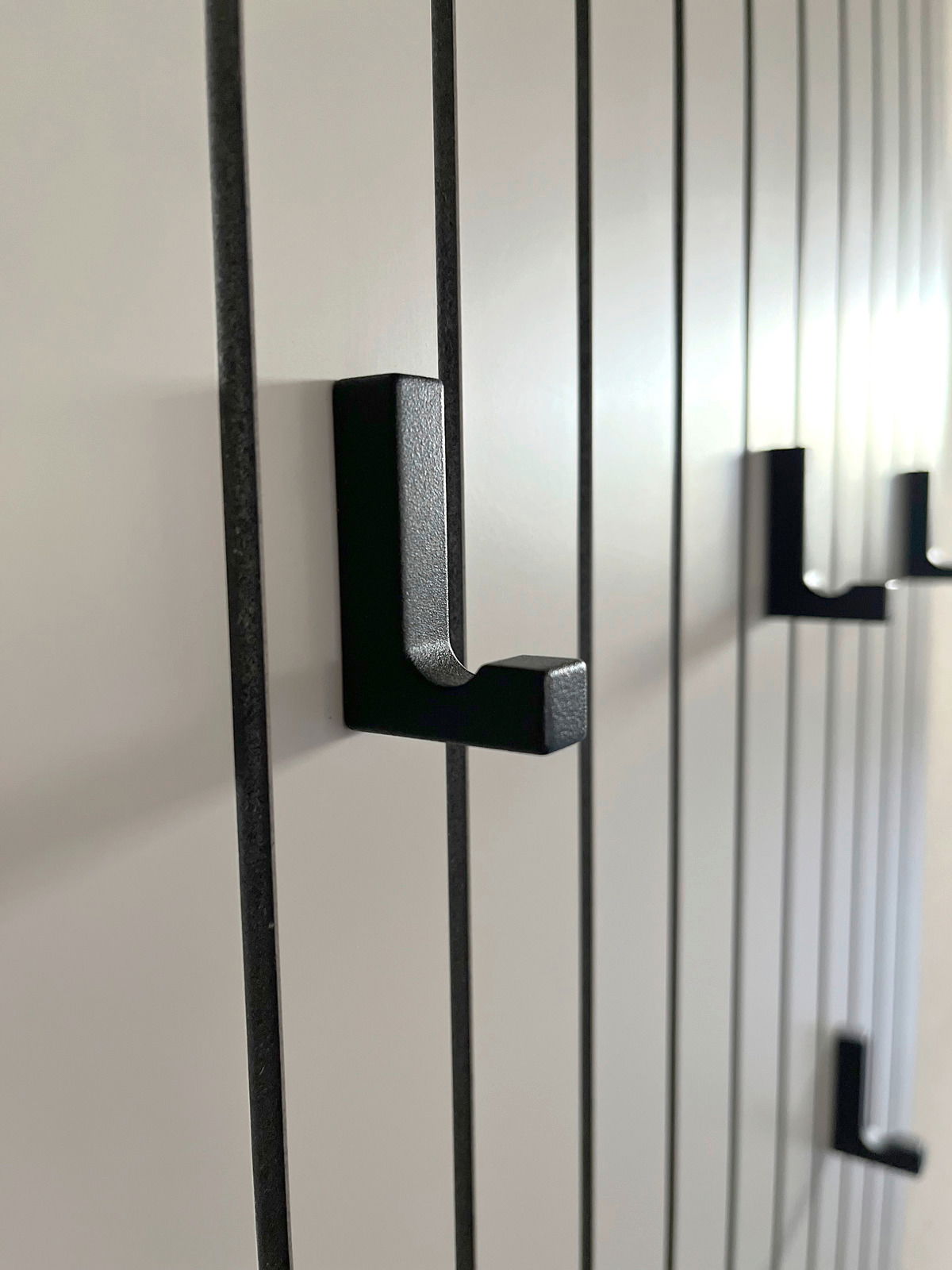 Nahaufnahme eines Garderobenpaneels mit schwarzen Haken auf vertikalen Streifen, seitliche Perspektive.
