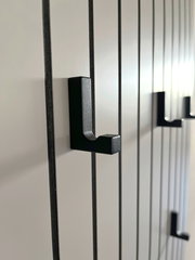 Nahaufnahme eines Garderobenpaneels mit schwarzen Haken auf vertikalen Streifen, seitliche Perspektive.
