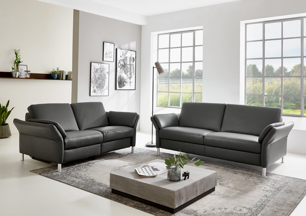 Dieter Knoll Sofa 3er LATINA L Zwei graue Sofas der Serie Dieter Knoll Sofa LATINA L in einem modernen Wohnzimmer, frontal betrachtet, mit großen Fenstern im Hintergrund.