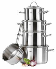 Stapel von glänzenden Edelstahl-Töpfen mit Deckel, seitliche Perspektive, umgeben von frischen Zutaten wie Zwiebeln und Knoblauch.