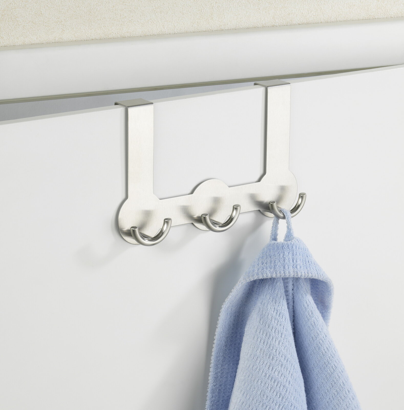 Edelstahl Türgarderobe Rondo mit vier Haken, frontal an einer Tür montiert, mit einem blauen Handtuch.