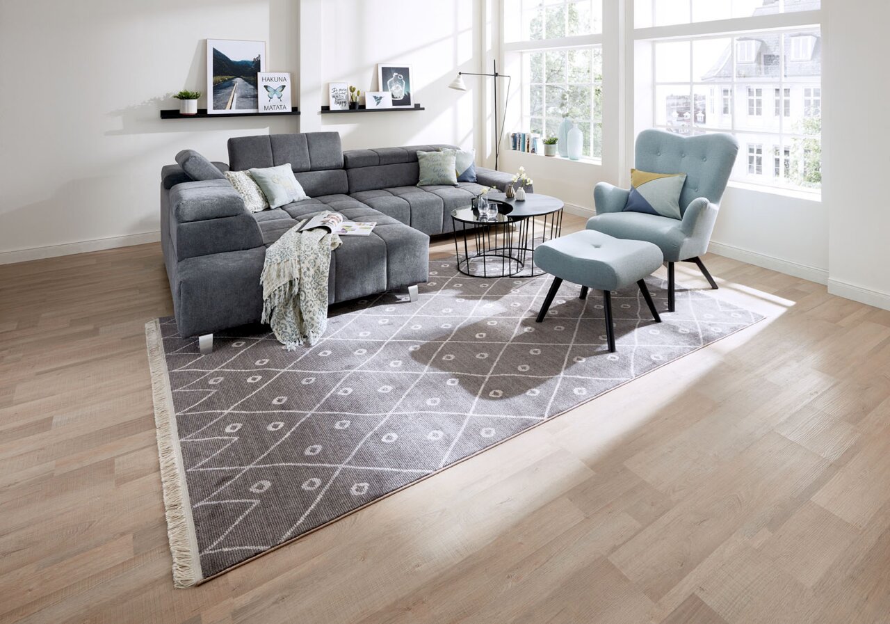 Wohnzimmer mit grauer Rundecke und hellblauem Sessel mit Hocker, aus der Perspektive von vorne rechts betrachtet.