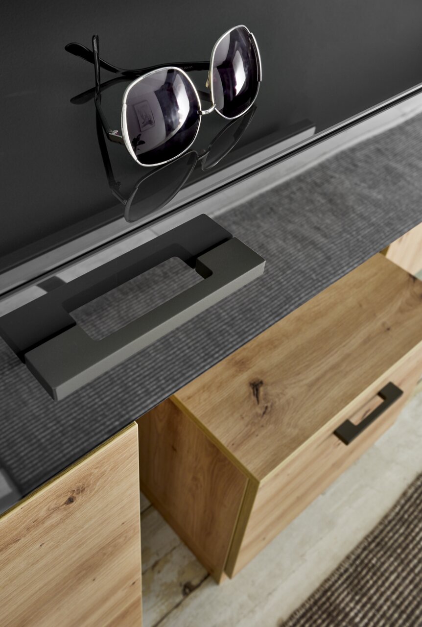 Nahaufnahme eines modernen Garderoben-Sets mit Holzschubladen und schwarzer Glasoberfläche, auf der eine Sonnenbrille liegt. Perspektive von oben.