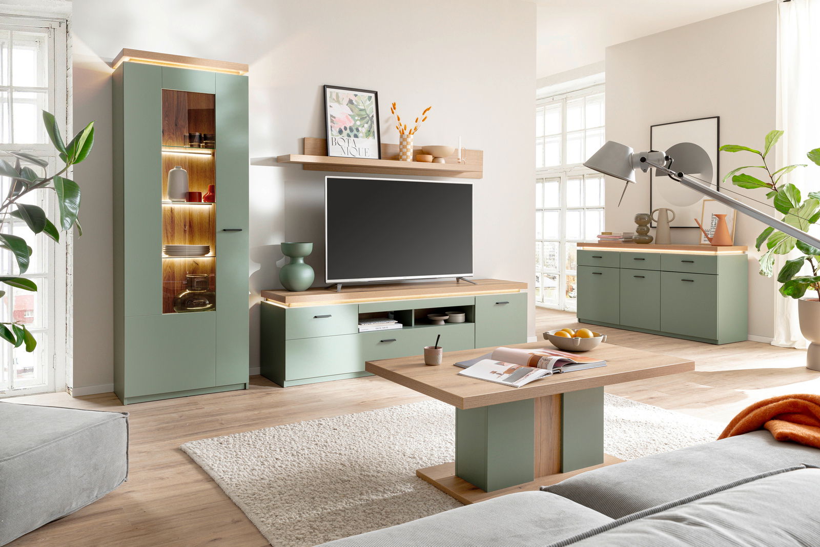 Modernes TV-Lowboard in einem stilvollen Wohnzimmer, frontal betrachtet, mit grünen Schränken und Holzakzenten.