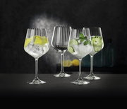 Vier elegante Gin Tonic Gläser, gefüllt mit Eis und verschiedenen Garnituren, auf einer dunklen Oberfläche vor einem stilvollen Hintergrund. Perspektive: seitlich.