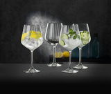Vier elegante Gin Tonic Gläser, gefüllt mit Eis und verschiedenen Garnituren, auf einer dunklen Oberfläche vor einem stilvollen Hintergrund. Perspektive: seitlich.