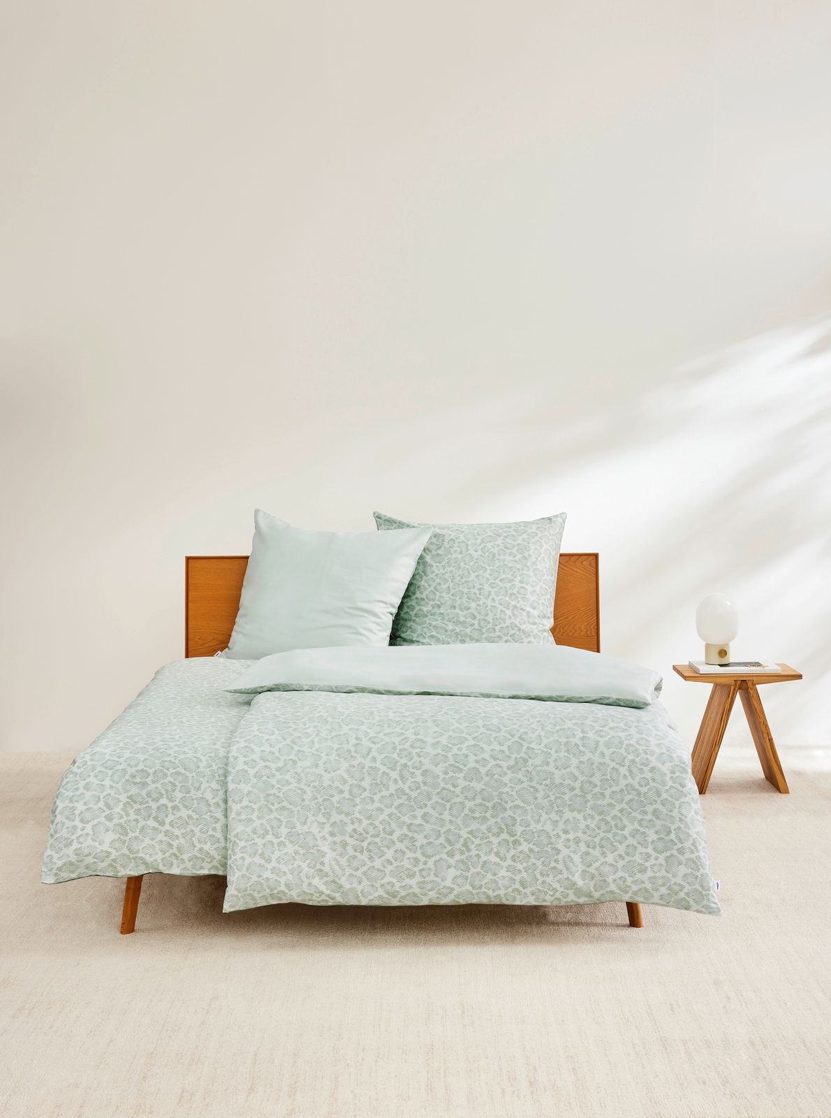 Satinbettwäsche 155x220cm in sanftem Grün mit dezentem Muster, auf einem Bett mit Holzrahmen, seitliche Perspektive