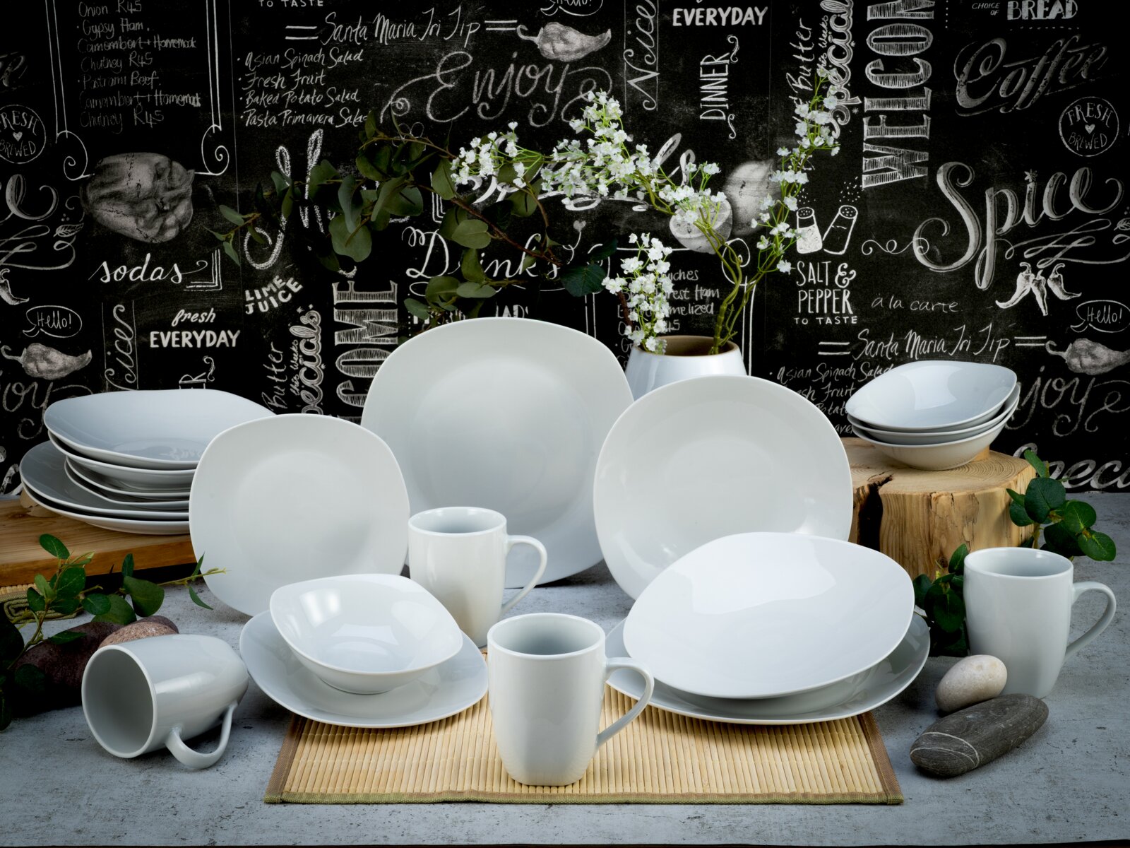 Creatable Kombiservice 20-tlg SQUARE Weißes Porzellan-Geschirrset mit Tellern, Schalen und Bechern auf dekorativem Tisch-Arrangement vor Tafelwand mit Schriftzügen, frontal aus leicht erhöhter Perspektive fotografiert.