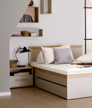 Nachtkommode in einem modernen Schlafzimmer, seitliche Perspektive, neben einem Bett mit Kissen und einer Lampe.