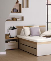 Nachtkommode in einem modernen Schlafzimmer, seitliche Perspektive, neben einem Bett mit Kissen und einer Lampe.