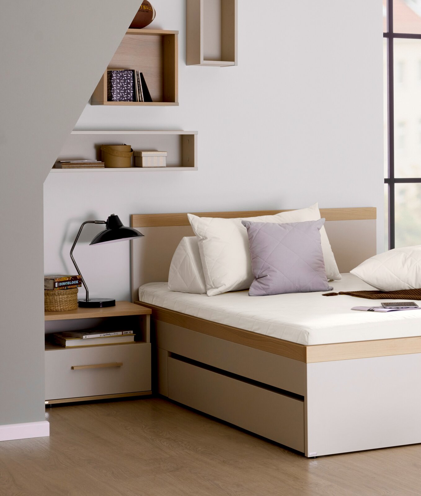 Paidi Nachtkommode MALIO Nachtkommode in einem modernen Schlafzimmer, seitliche Perspektive, neben einem Bett mit Kissen und einer Lampe.