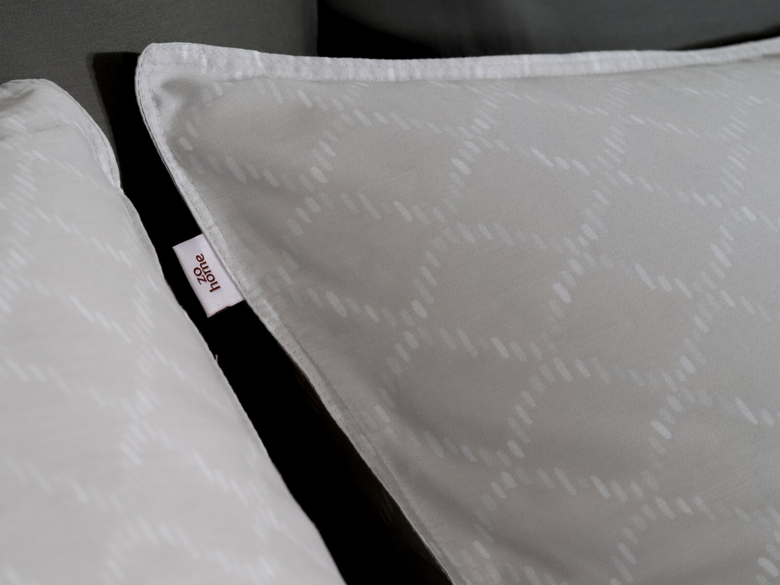 ZO!HOME Beddengoed LINEA DI SATINADO Close-up van ZO!HOME-beddengoed LINEA DI SATINADO met subtiel patroon en label, zijaanzicht