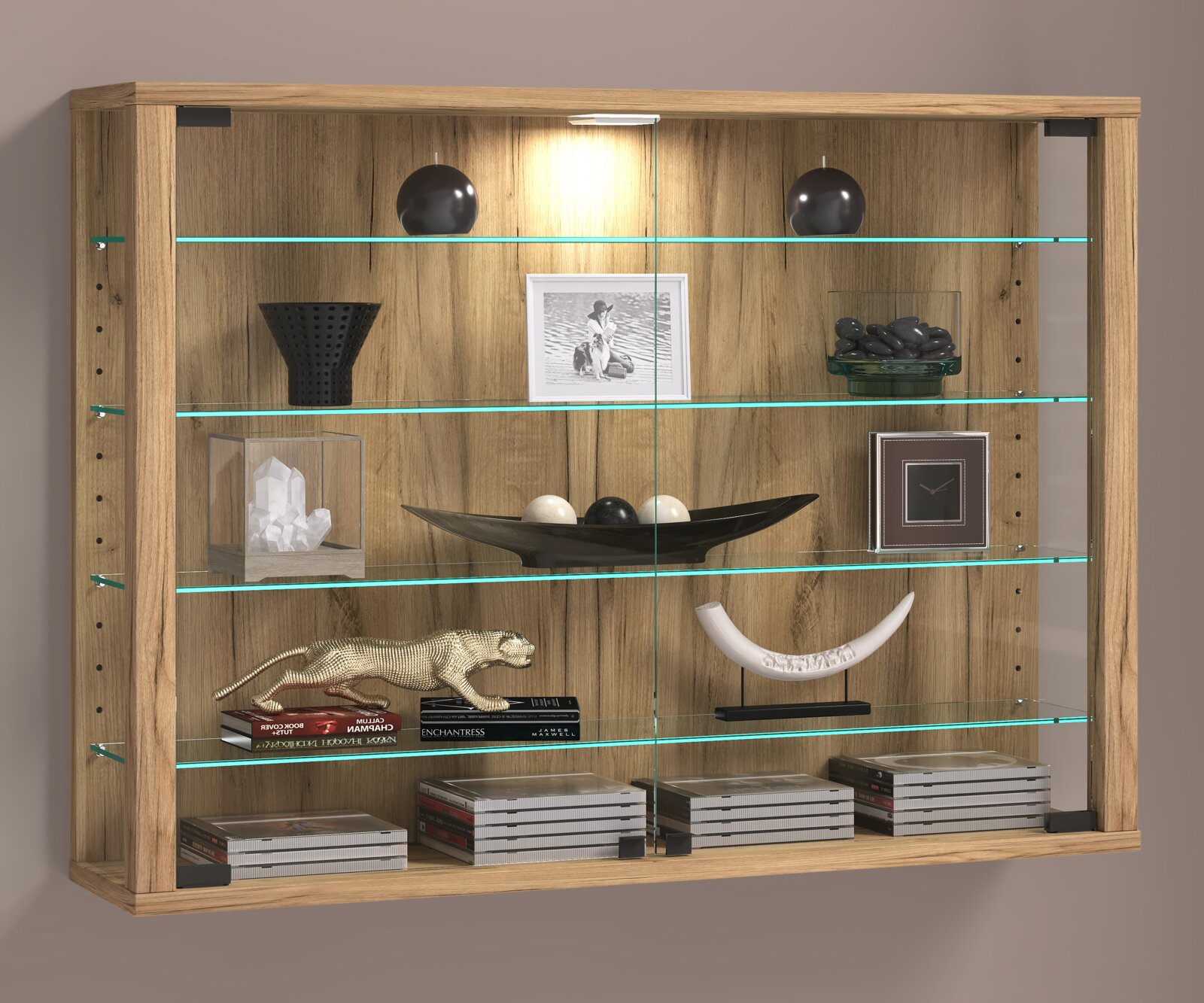 Wandhängende Vitrine aus Holzoptik mit Glasböden und integrierter LED-Beleuchtung, dekoriert mit Vasen, Schalen, Büchern und CDs, frontal aus leichter Untersicht fotografiert.