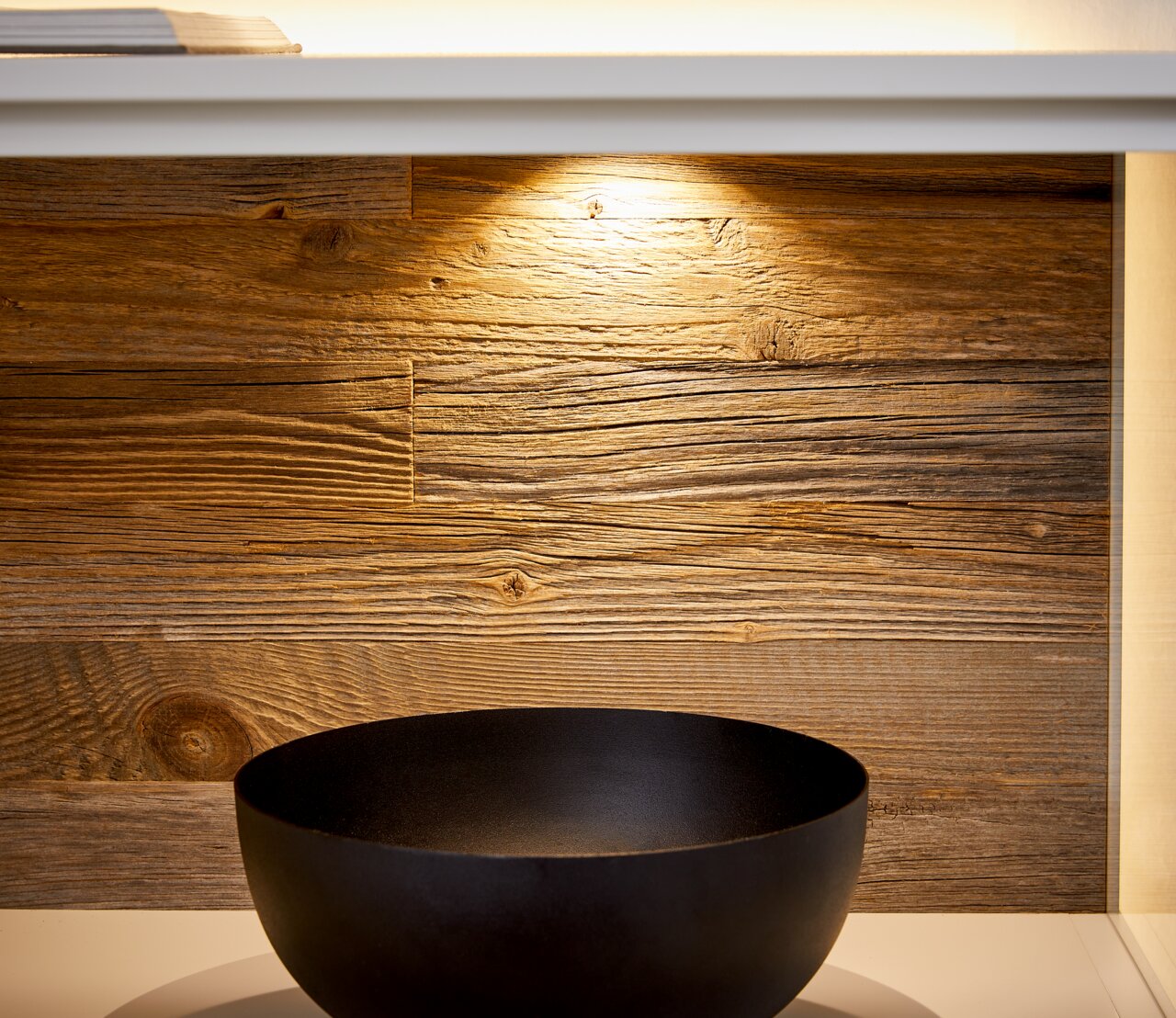 Nahaufnahme eines Sideboards mit Holzrückwand und schwarzer Schale, von vorne betrachtet.