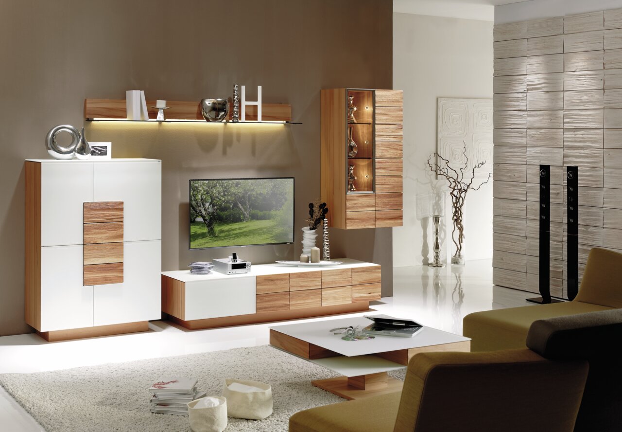 Moderne Wohnwand VMONTANARA von Voglauer in einer stilvollen Wohnzimmerumgebung, frontal betrachtet. Die Kombination aus Holz und weißen Elementen verleiht dem Raum eine elegante und zeitgemäße Atmosphäre.