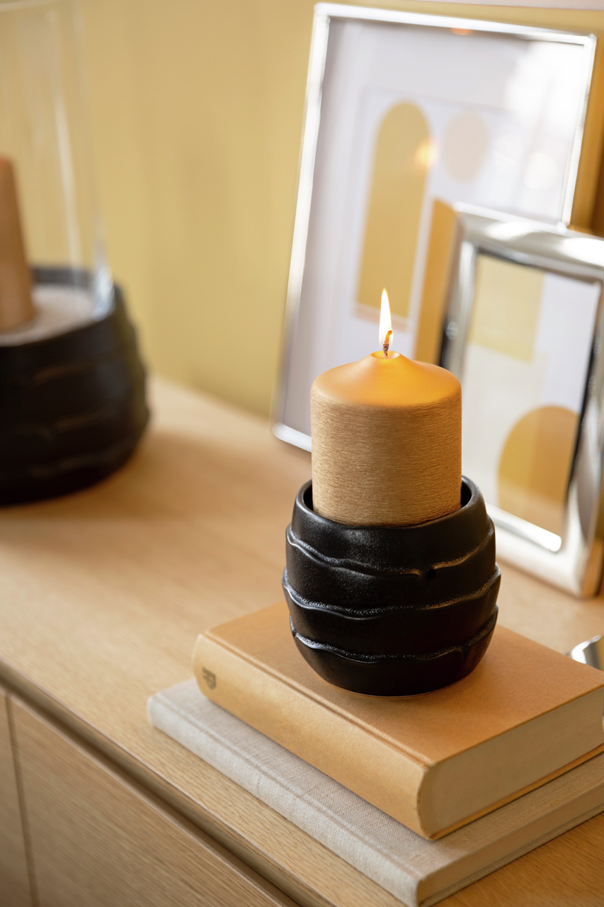 Kerzenhalter aus Keramik mit brennender Kerze, seitliche Perspektive auf einem Tisch mit Büchern und Bilderrahmen im Hintergrund.