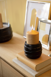 Kerzenhalter aus Keramik mit brennender Kerze, seitliche Perspektive auf einem Tisch mit Büchern und Bilderrahmen im Hintergrund.