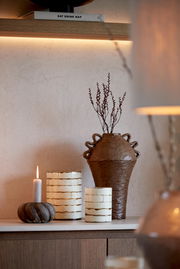 Stimmungsvolle Szene mit brennendem Teelicht in einem rustikalen Kerzenhalter, umgeben von dekorativen Vasen und Zweigen, seitliche Perspektive.