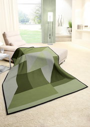 Grüne Wohndecke mit geometrischem Muster auf einem cremefarbenen Teppich in einem modernen Wohnzimmer, seitliche Perspektive.