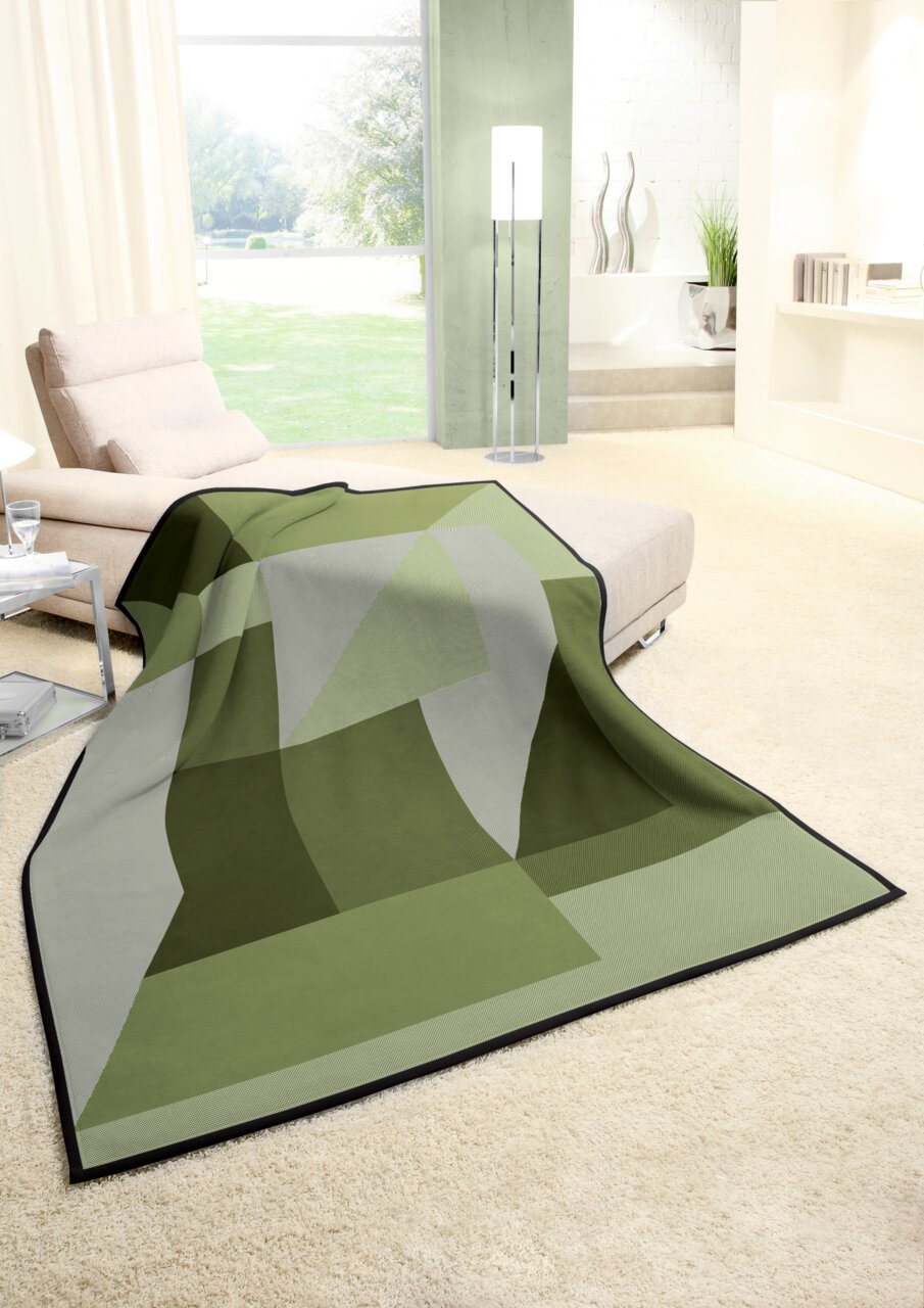 biederlack Wohndecke COTTON HOME Grüne Wohndecke mit geometrischem Muster auf einem cremefarbenen Teppich in einem modernen Wohnzimmer, seitliche Perspektive.