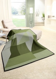 Grüne Wohndecke mit geometrischem Muster auf einem cremefarbenen Teppich in einem modernen Wohnzimmer, seitliche Perspektive.