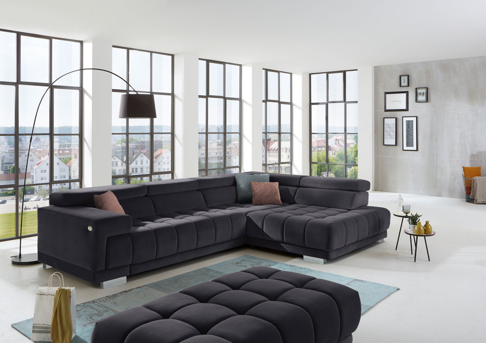 Beldomo Speed Ecksofa SPLIFF S Modernes Ecksofa in dunklem Stoff in einem hellen Wohnzimmer mit großen Fenstern, seitliche Perspektive.