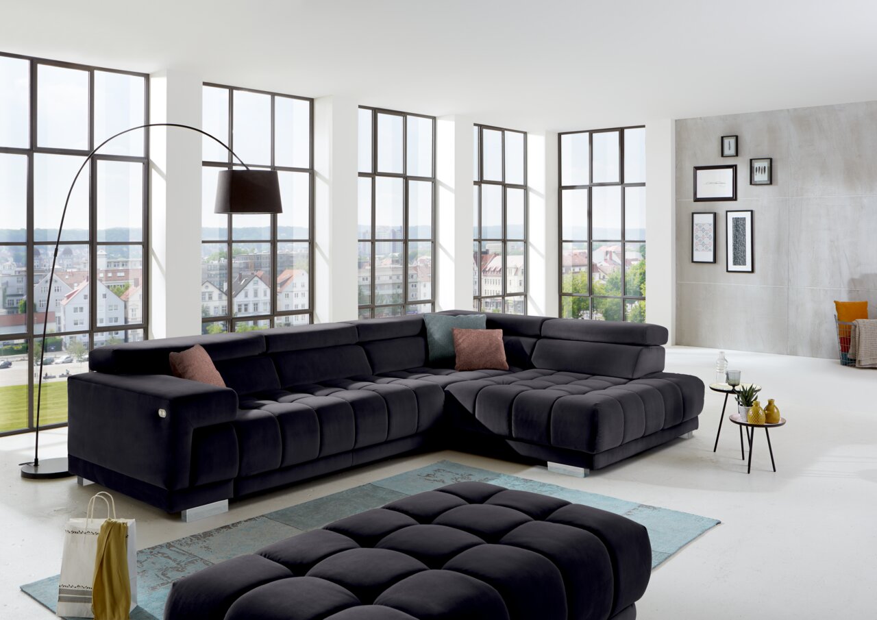 Beldomo Speed Ecksofa SPLIFF S Modernes Ecksofa in dunklem Stoff in einem hellen Wohnzimmer mit großen Fenstern, seitliche Perspektive.