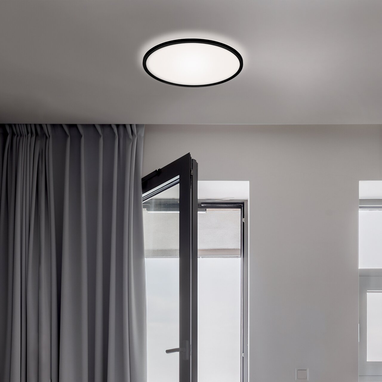 Moderne LED-Deckenleuchte in einem Raum mit geöffneter Tür und Vorhängen, von unten betrachtet.