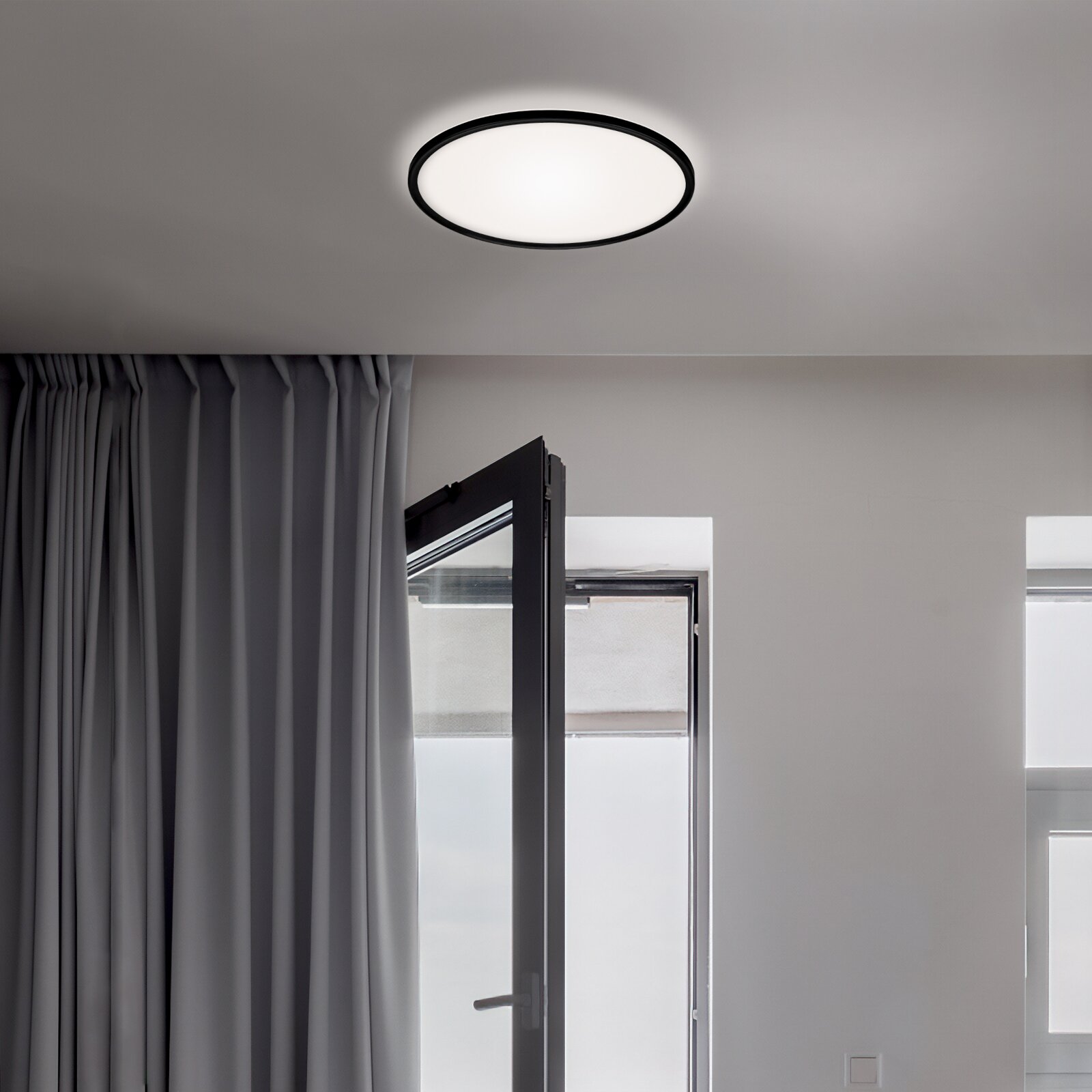 Moderne LED-Deckenleuchte in einem Raum mit geöffneter Tür und Vorhängen, von unten betrachtet.