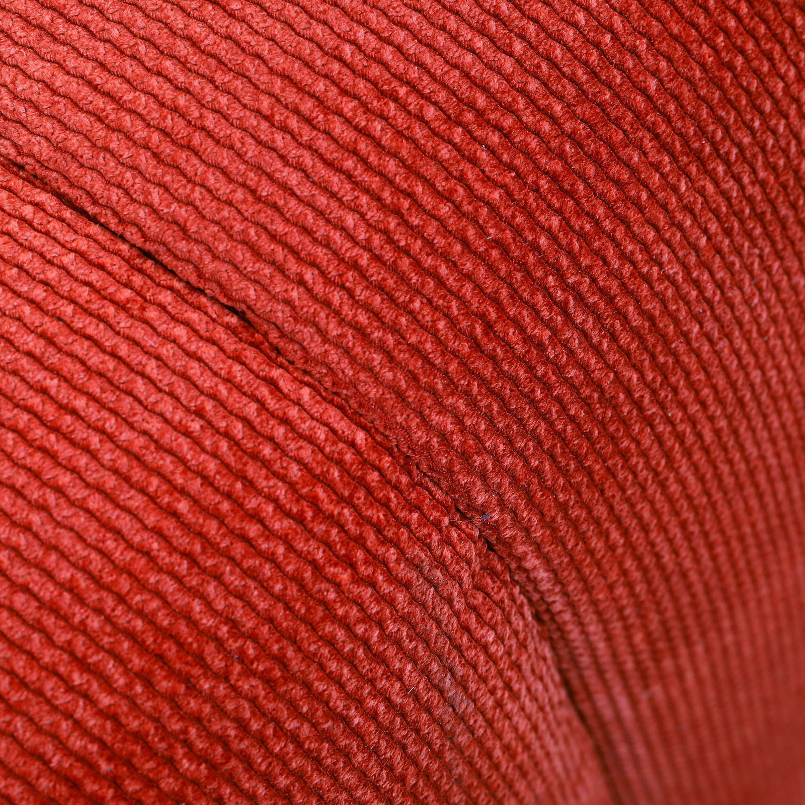 Nahaufnahme eines roten, gerippten Stoffes, vermutlich Teil eines Hockers, aus seitlicher Perspektive.