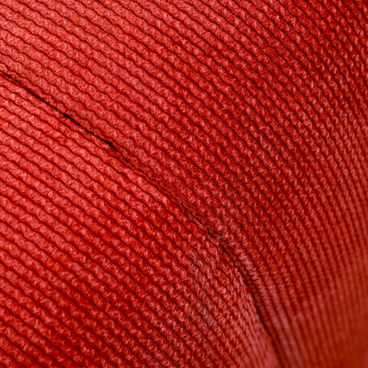 Nahaufnahme eines roten, gerippten Stoffes, vermutlich Teil eines Hockers, aus seitlicher Perspektive.