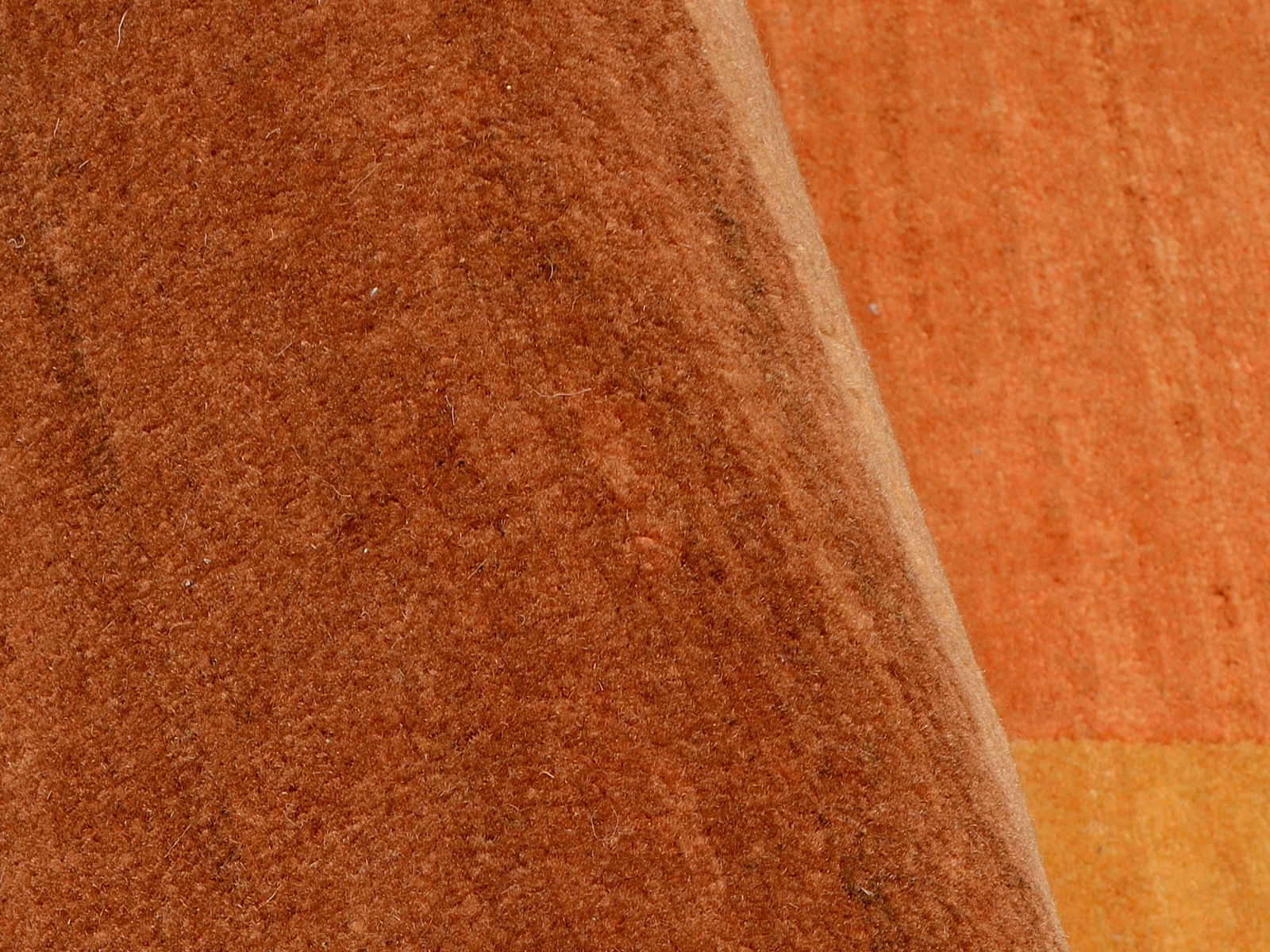 Nahaufnahme eines orangefarbenen Teppichs mit weicher Textur, teilweise aufgerollt.