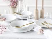 Heller, elegant gedeckter Tisch mit weißen, geriffelten Porzellantellern und Schalen, goldfarbenem Besteck sowie Wein- und Wassergläsern; Perspektive: leicht erhöht und frontal aus Tischhöhe.