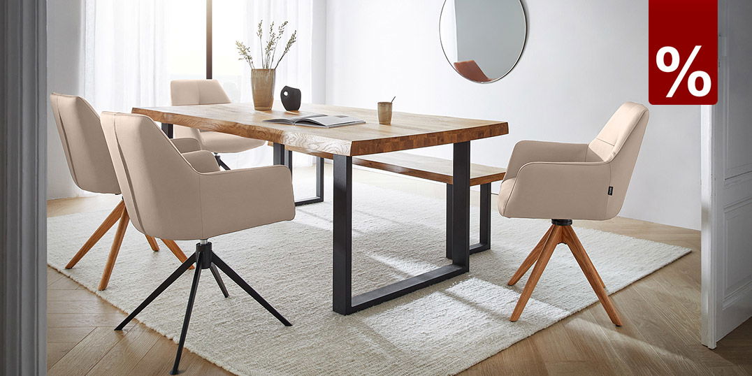 Helles Esszimmer mit Holztisch, vier beigen Drehstühlen, Teppich und rundem Wandspiegel