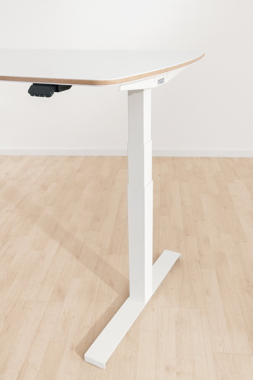 Modern, in hoogte verstelbaar bureau in zijaanzicht, met een wit tafelblad en een stevig metalen onderstel op een houten vloer.
