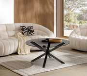 Moderner Couchtisch mit schwarzer Glasplatte und gekreuztem Metallgestell, seitliche Perspektive, in einem stilvollen Wohnzimmer mit beigen Sofas und großen Fenstern.