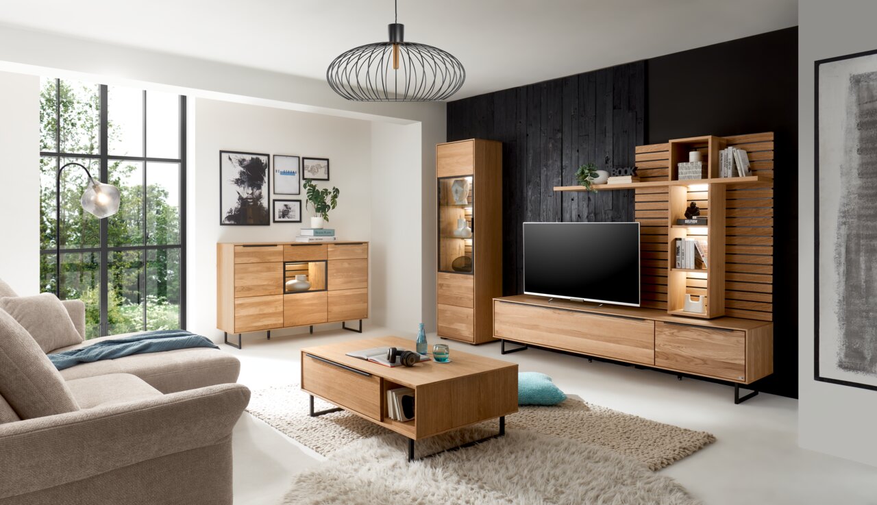 Moderne Wohnzimmermöbel in Holzoptik, bestehend aus einem Sideboard, einer Vitrine, einem TV-Lowboard und einem Couchtisch, aus der Perspektive eines gemütlichen Wohnzimmers mit großen Fenstern und stilvoller Dekoration.