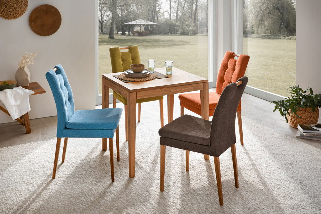 Esszimmer mit einem Holztisch und bunten Stühlen aus der Serie BARCELONA, Perspektive von schräg oben.