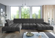 Große, moderne Polsterrundecke in dunklem Grau, perspektivisch von vorne fotografiert, in einem hellen Wohnzimmer mit großen Fenstern und stilvoller Dekoration.