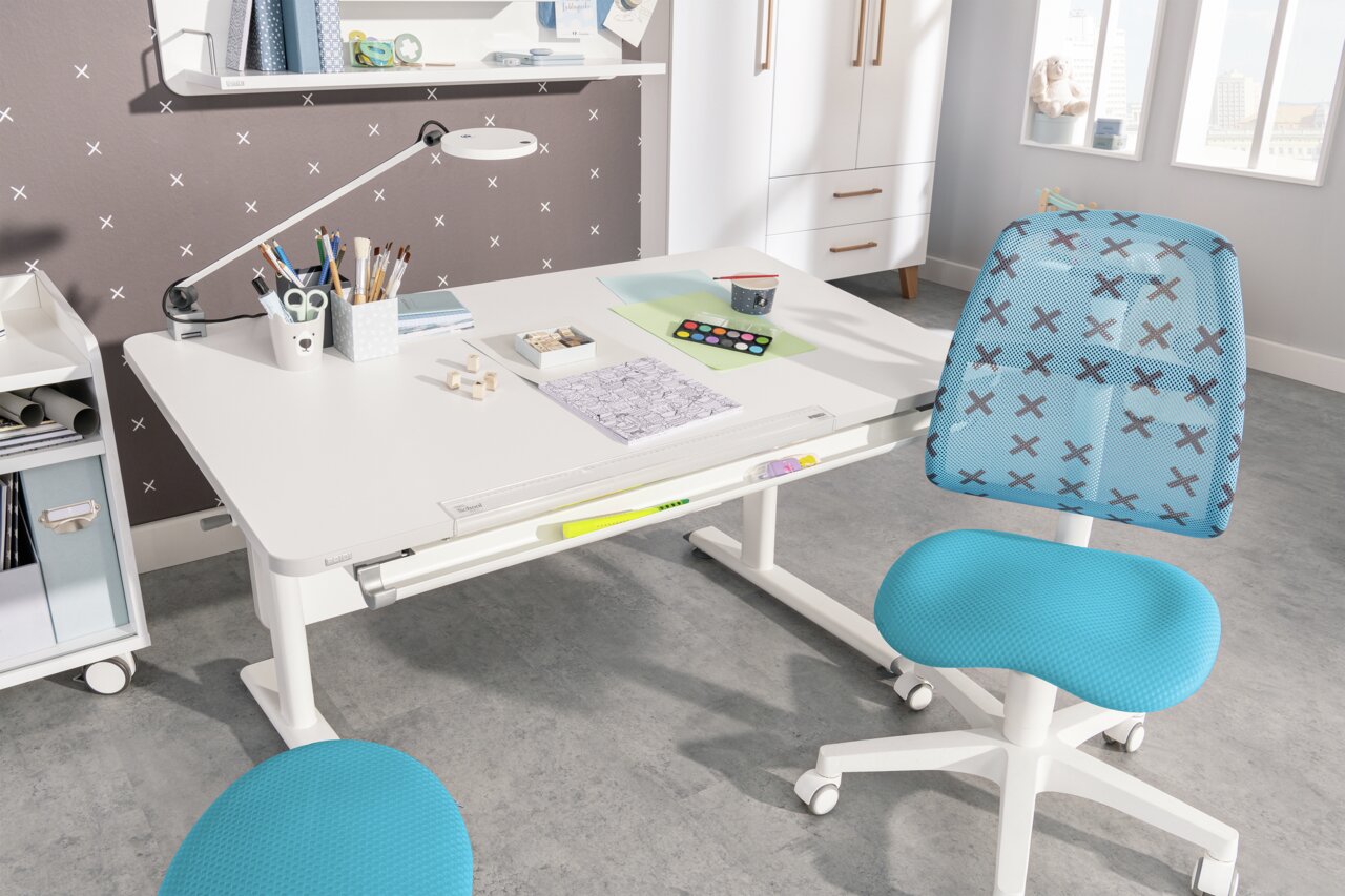 Moderne draaistoel voor jongeren in blauw met ruitpatroon, gezien vanaf de zijkant, voor een wit bureau in een lichte ruimte.