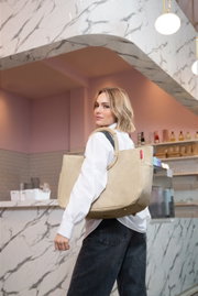 Een jonge vrouw in een café draagt een grote beige corduroy draagtas met brede hengsels over haar schouder; perspectief: licht van opzij van achteren, met de focus op de tas.