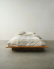 Bett mit Bettwäsche in neutralen Tönen, fotografiert aus der Vorderansicht in einem minimalistischen Raum.