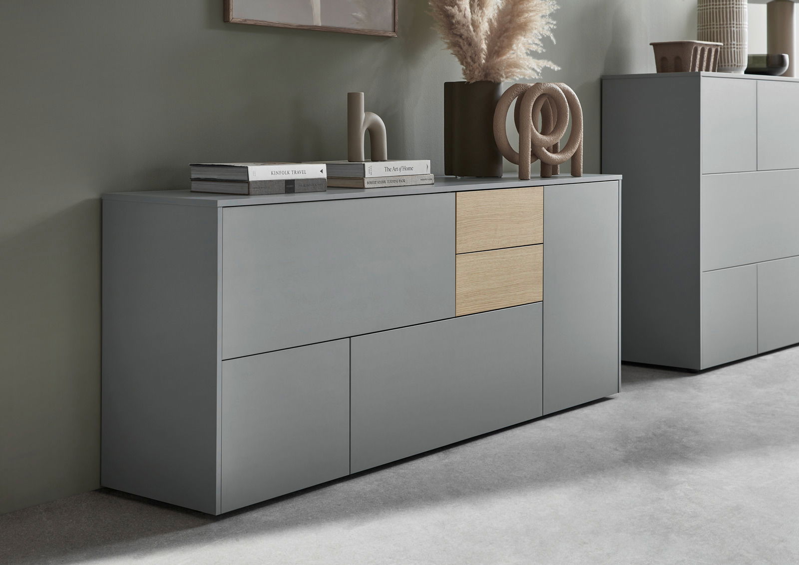 Modernes Sideboard in Grau mit zwei Holzelementen, dekoriert mit Büchern und Skulpturen, seitliche Perspektive.