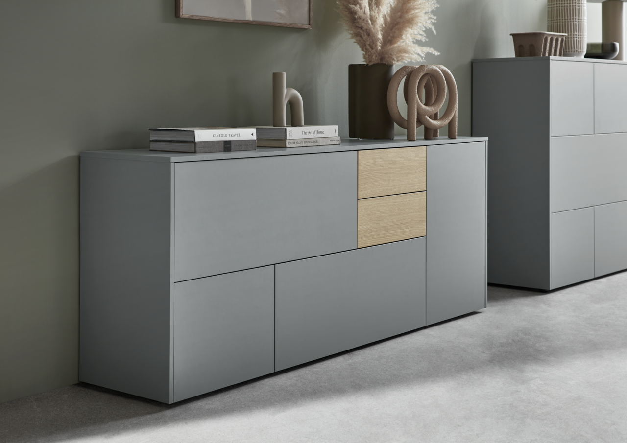 Modernes Sideboard in Grau mit zwei Holzelementen, dekoriert mit Büchern und Skulpturen, seitliche Perspektive.