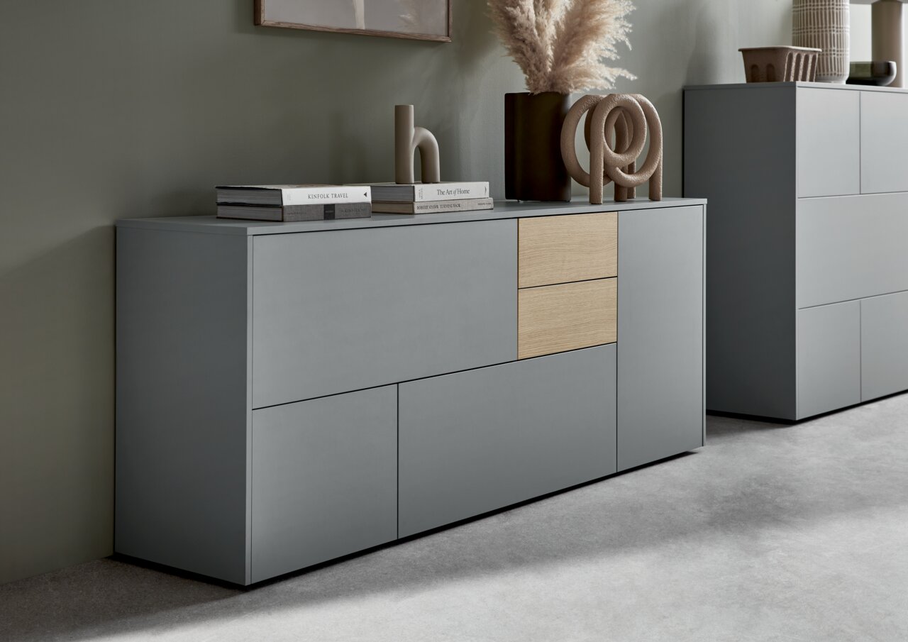 Modernes Sideboard in Grau mit zwei Holzelementen, dekoriert mit Büchern und Skulpturen, seitliche Perspektive.